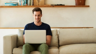 Mann sitzt auf dem Sofa mit offenem Laptop